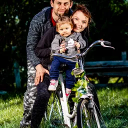 Rodzina z małym dzieckiem na rowerze ozdobionym kwiatami, pozująca na tle zieleni.