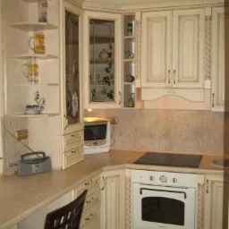Klasyczna kuchnia z kremowymi szafkami z frezowanymi frontami i witryną z motywem roślinnym, uzupełniona o mikrofalówkę i radio na blacie.