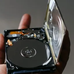 Otwarty dysk twardy trzymany w dłoni, widoczne talerze i elementy wewnętrzne, prawdopodobnie w trakcie analizy lub demontażu.