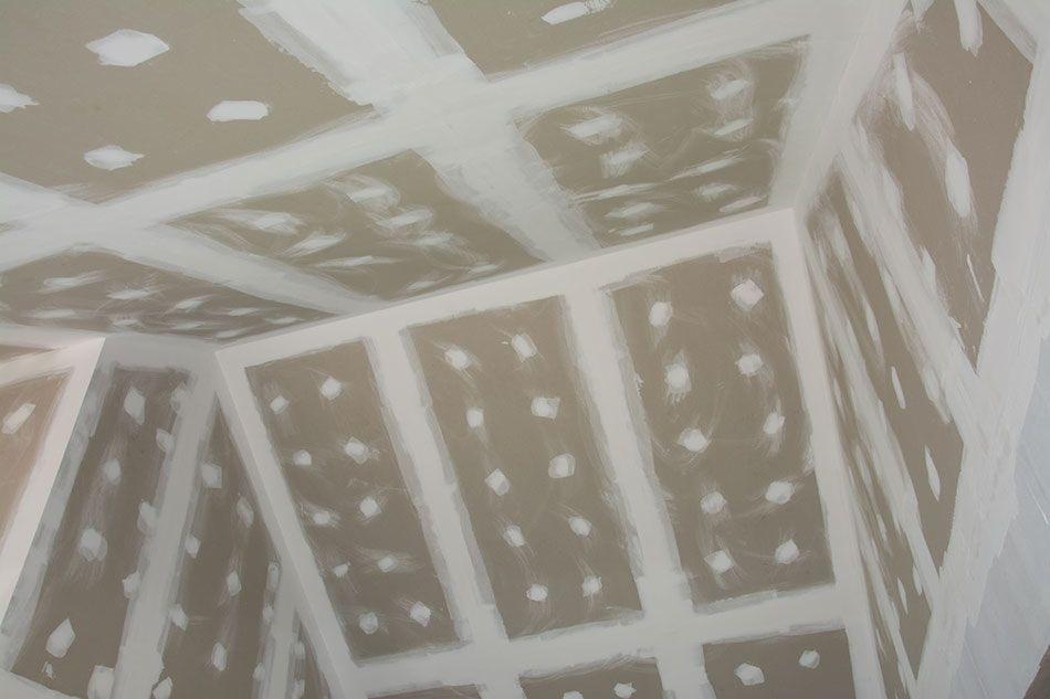 Wnętrze w trakcie prac wykończeniowych: ściany i sufit pokryte płytami kartonowo-gipsowymi, łączenia i wkręty zaszpachlowane na biało.