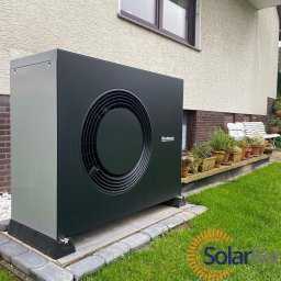 Solar Kontakt - Czarna pompa ciepła Buderus, zamontowana przy ścianie domu z beżowym tynkiem, widoczna na tle zielonego trawnika i dekoracyjnych kamieni.