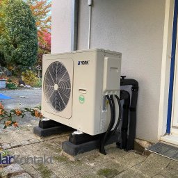 Solar Kontakt - Zamontowana pompa ciepła York na betonowych podstawach, widoczne czarne rury przy elewacji budynku. Tło: jesienne drzewa i fragment ogrodu.