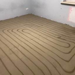 Solar Kontakt - Układanie rur ogrzewania podłogowego w spiralnym wzorze w pomieszczeniu w Kielcach. Widoczne szare rury zatopione w wylewce.