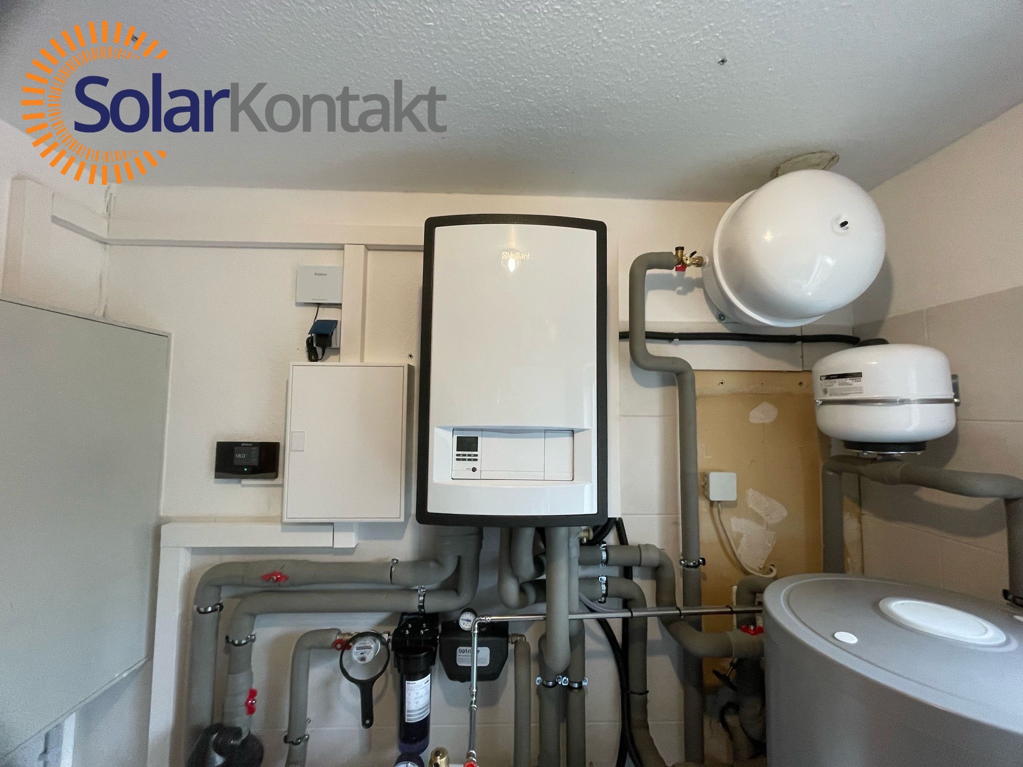Kotłownia z nowoczesnym kotłem gazowym Vaillant, zbiornikami i rurami. Instalacja grzewcza w pomieszczeniu z logo SolarKontakt w lewym górnym rogu.