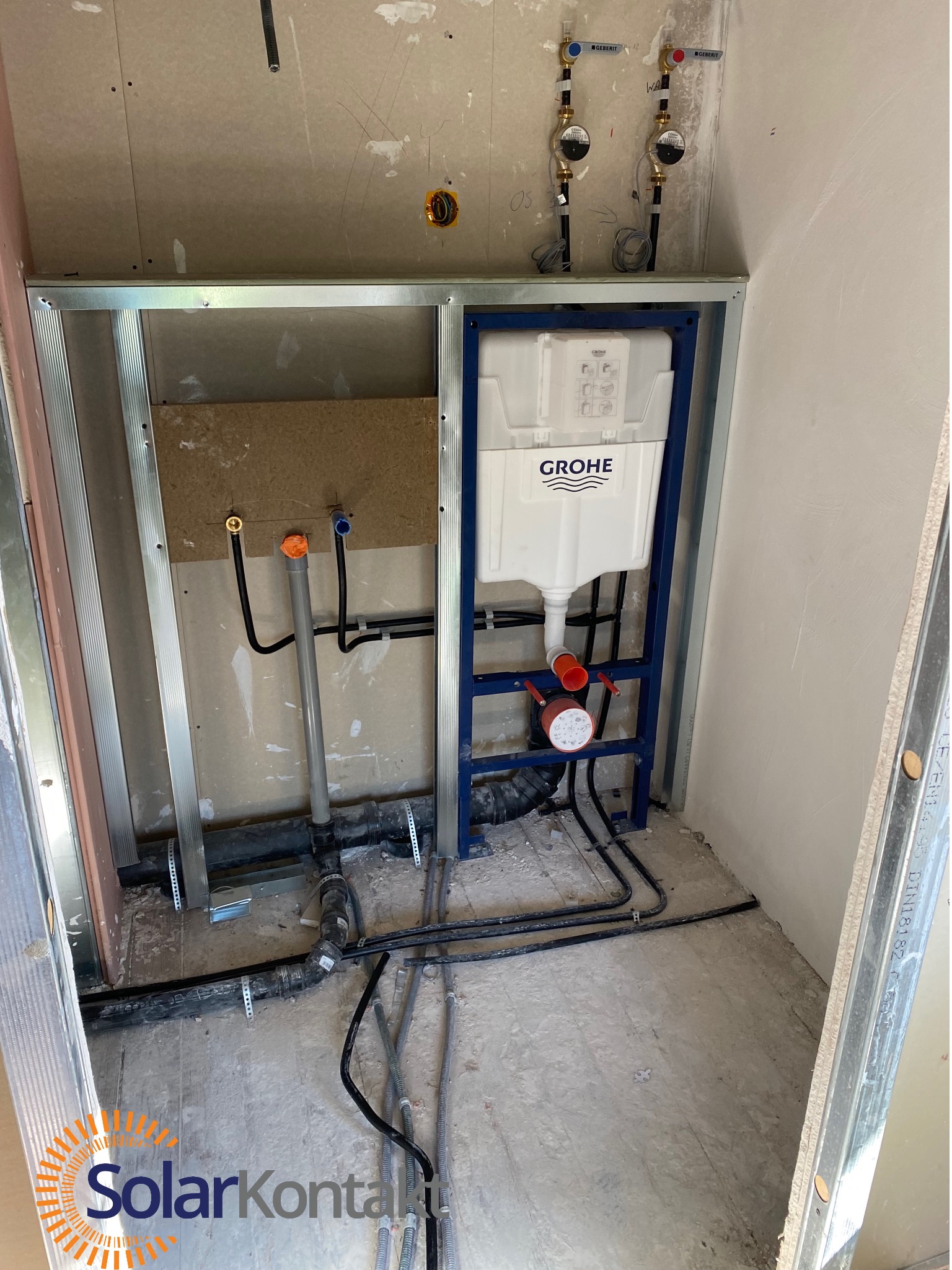 Instalacja podtynkowa WC Grohe w trakcie montażu, widoczne rury, stelaż i liczniki wody. Ściany w surowym stanie, widoczne profile montażowe.