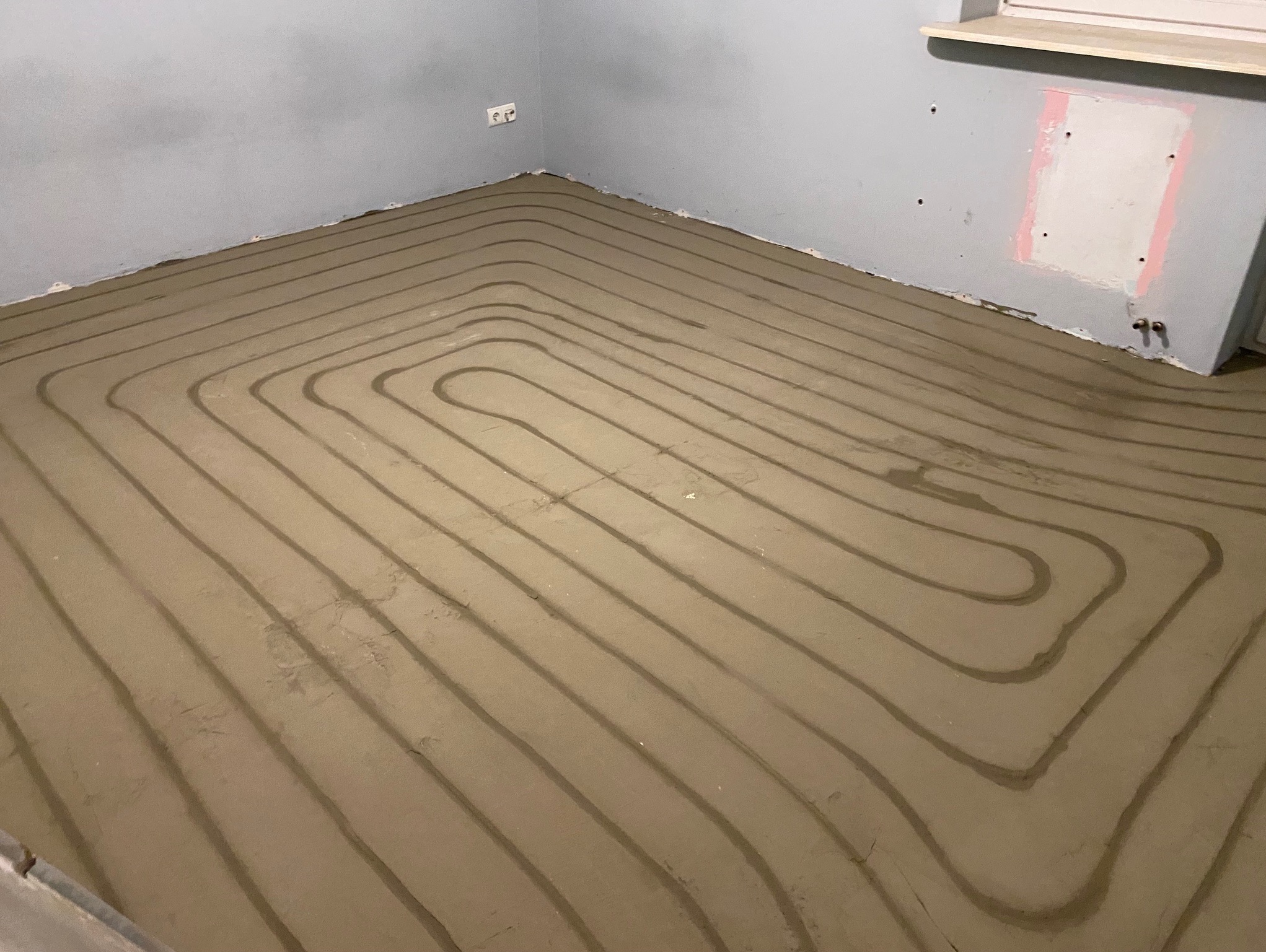 Układanie rur ogrzewania podłogowego w spiralnym wzorze w pomieszczeniu w Kielcach. Widoczne szare rury zatopione w wylewce.