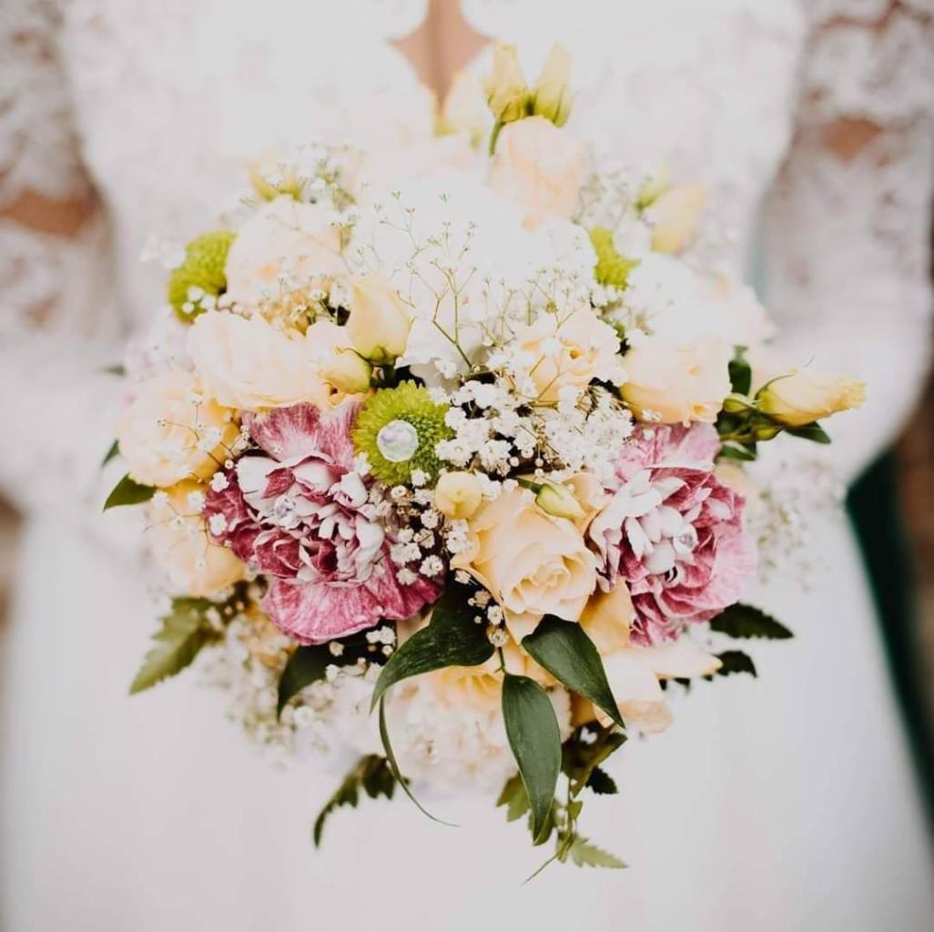 Bukiet ślubny z różowych i żółtych róż trzymany przez osobę w białej koronkowej sukni, sfotografowany w Opocznie.