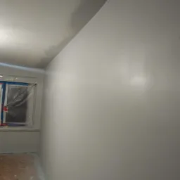 Świeżo pomalowane na szaro ściany i sufit w pokoju, okno zabezpieczone folią malarską, widoczne ślady po szpachlowaniu na suficie.