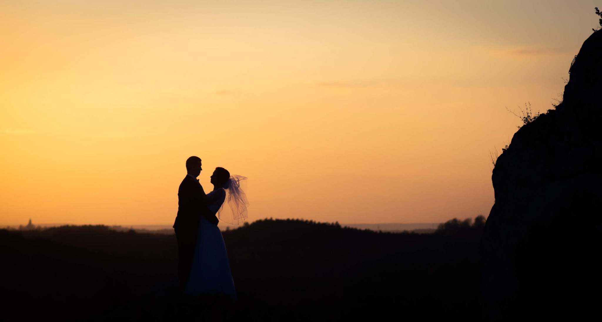 Silueta pary młodej na tle pomarańczowego zachodu słońca i skalistego wzgórza.