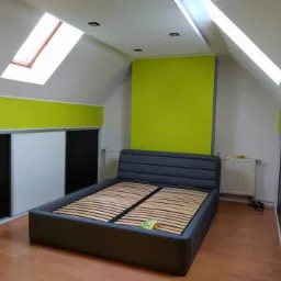 Pokój na poddaszu z łóżkiem na drewnianej podłodze, ściany pomalowane w dwóch odcieniach zieleni, z oknami dachowymi i szafą przesuwną.