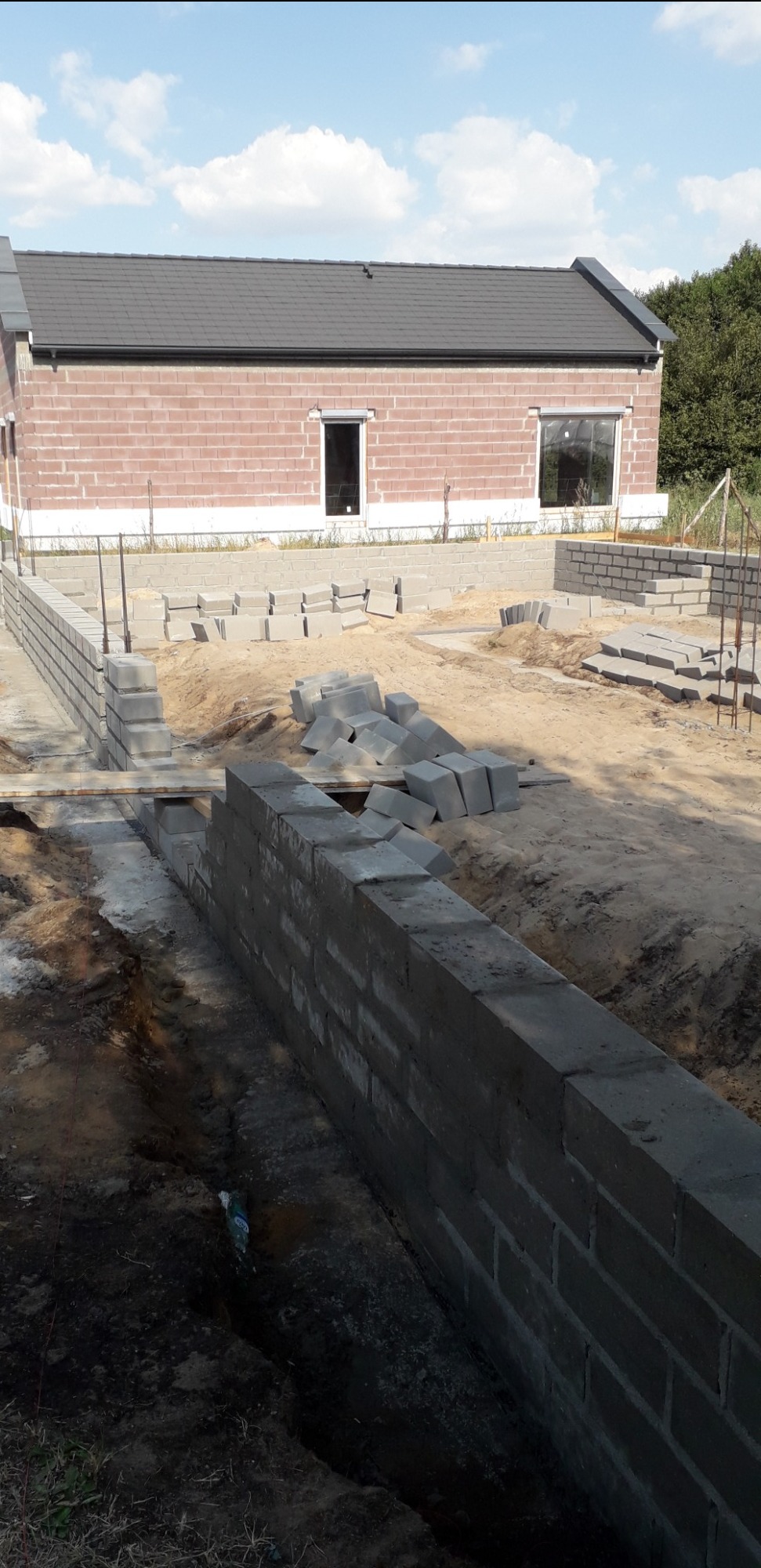 Wznoszenie fundamentów z bloczków betonowych pod budynek z cegły, widoczne zbrojenia i rozsypane bloczki na placu budowy.