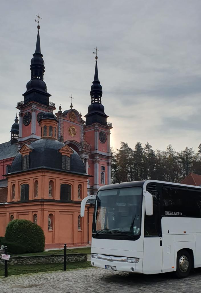 Biały autokar turystyczny na tle barokowej bazyliki w Krzeszowie, Dolny Śląsk.