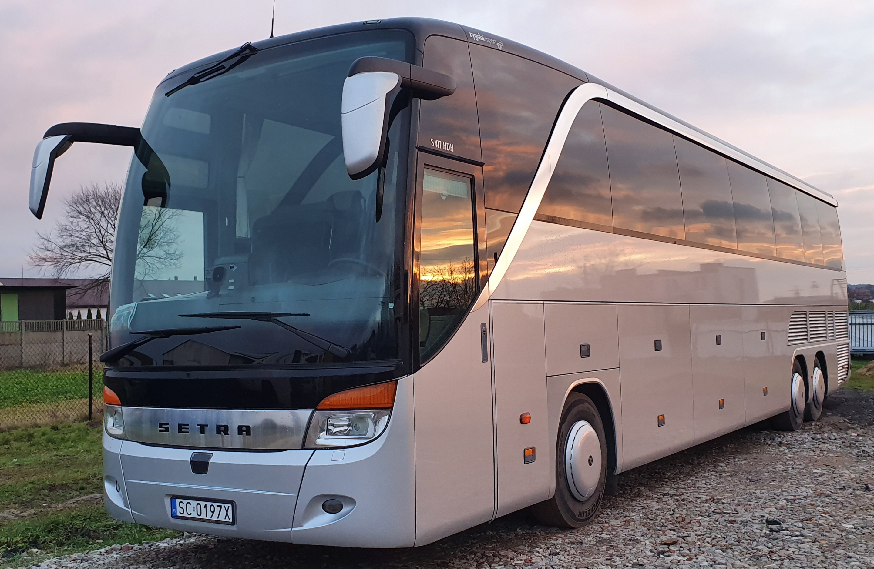Autokar marki Setra S 417 HDH z polską tablicą rejestracyjną, zaparkowany na żwirowym podłożu, z odbijającym się zachodem słońca w oknach.