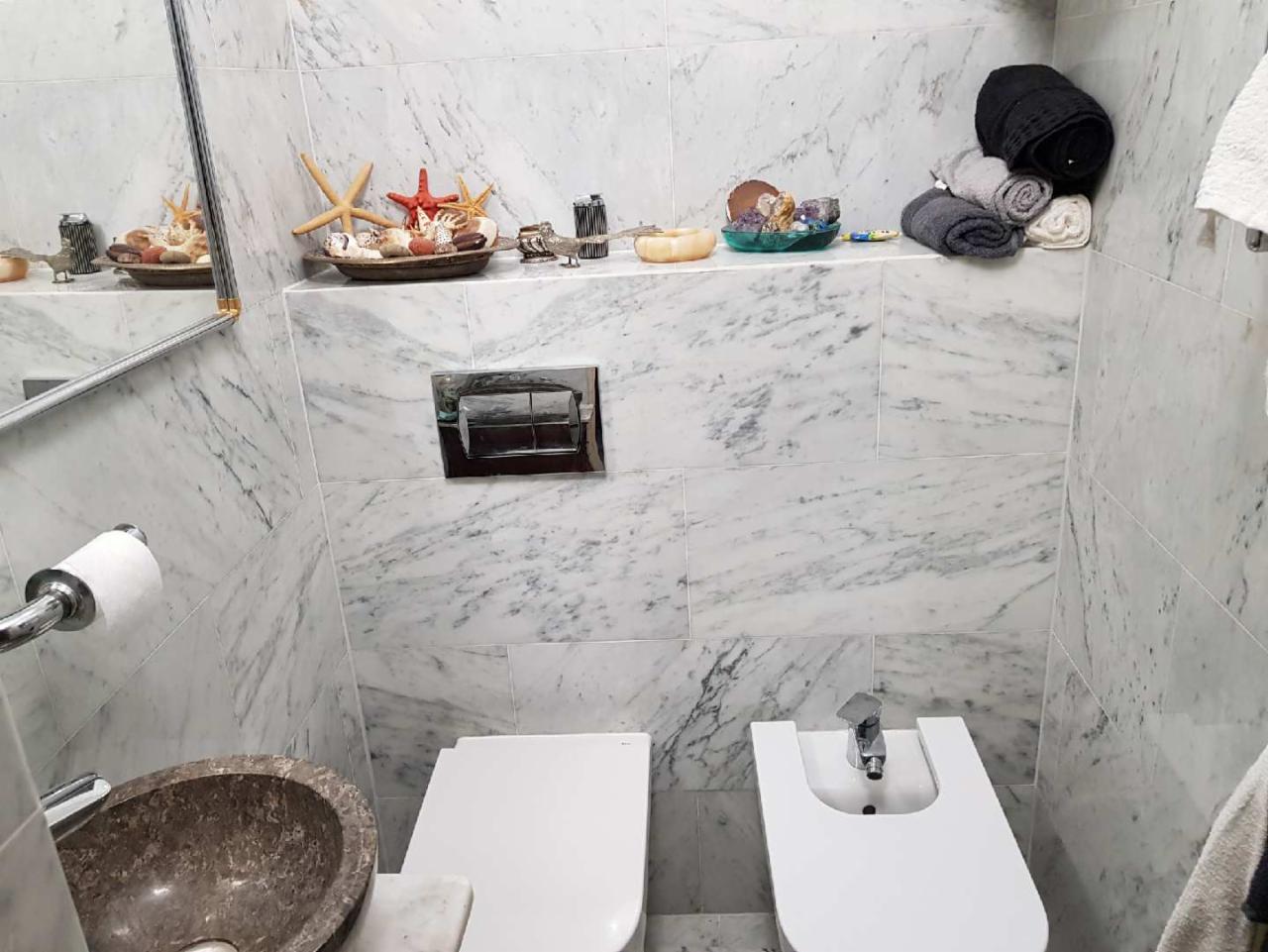 Wykończona łazienka z marmurowymi płytkami, dekorowana muszlami i rozgwiazdami na półce, z umywalką z kamienia i nowoczesną armaturą.