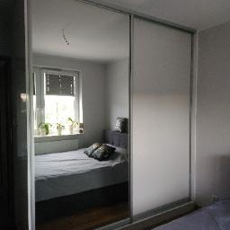 Kristol - Szafa przesuwna z lustrem i matową szybą, widok na sypialnię z łóżkiem i oknem.