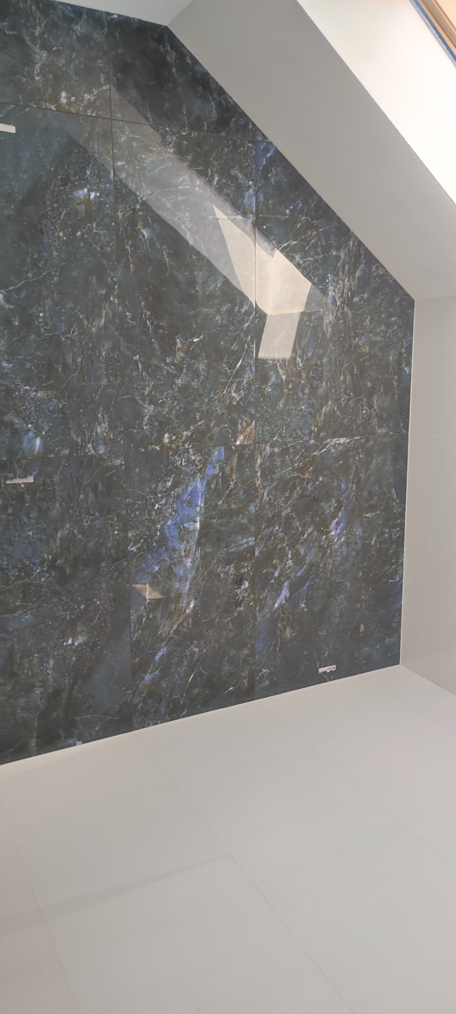 Ściana i podłoga wyłożone płytkami imitującymi marmur w odcieniach granatu i bieli, widoczne spoiny, pomieszczenie ze skosem.