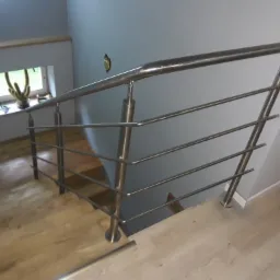 Nowoczesna, metalowa balustrada schodowa z poziomymi prętami w domu w Sanoku, widok z góry na drewniane schody.