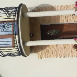 Elewacja domu z drewnianymi drzwiami wejściowymi, kamienną okładziną i balkonem z kutą balustradą, ozdobiona donicami z różowymi kwiatami.