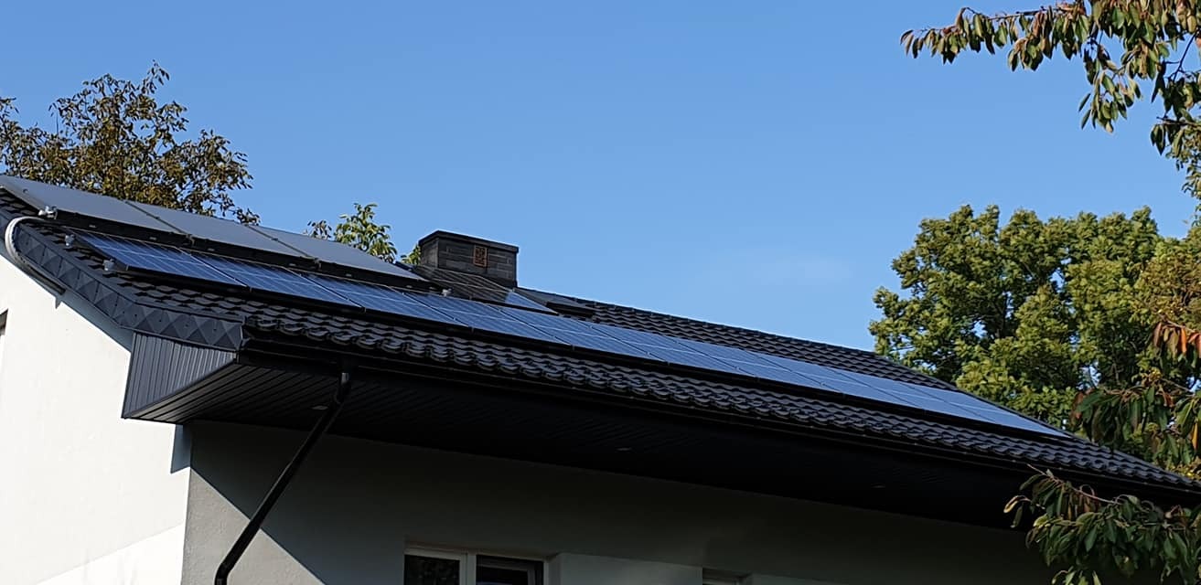 Panele fotowoltaiczne zamontowane na czarnym, spadzistym dachu domu jednorodzinnego w słoneczny dzień, widok z dołu.