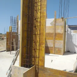 Żółte szalunki z widocznym zbrojeniem pionowym na budowie domu, w tle bloczki z betonu komórkowego.