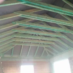 Konstrukcja drewniana dachu z membraną, widok od wewnątrz surowego budynku z czerwonej cegły.