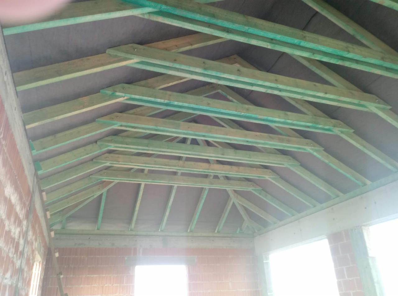 Konstrukcja drewniana dachu z membraną, widok od wewnątrz surowego budynku z czerwonej cegły.