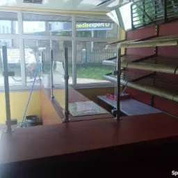 Pusta lada sklepowa z metalowymi przegrodami, regały bez towaru, widok na ulicę z rowerzystką za szybą.