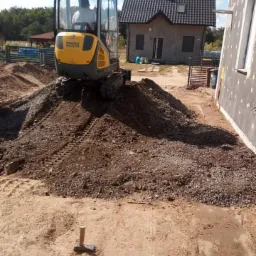 Mini koparka Wacker Neuson na usypanym wzgórzu ziemi i gruzu w Zielonej Górze, przygotowująca teren pod budowę lub prace ziemne.