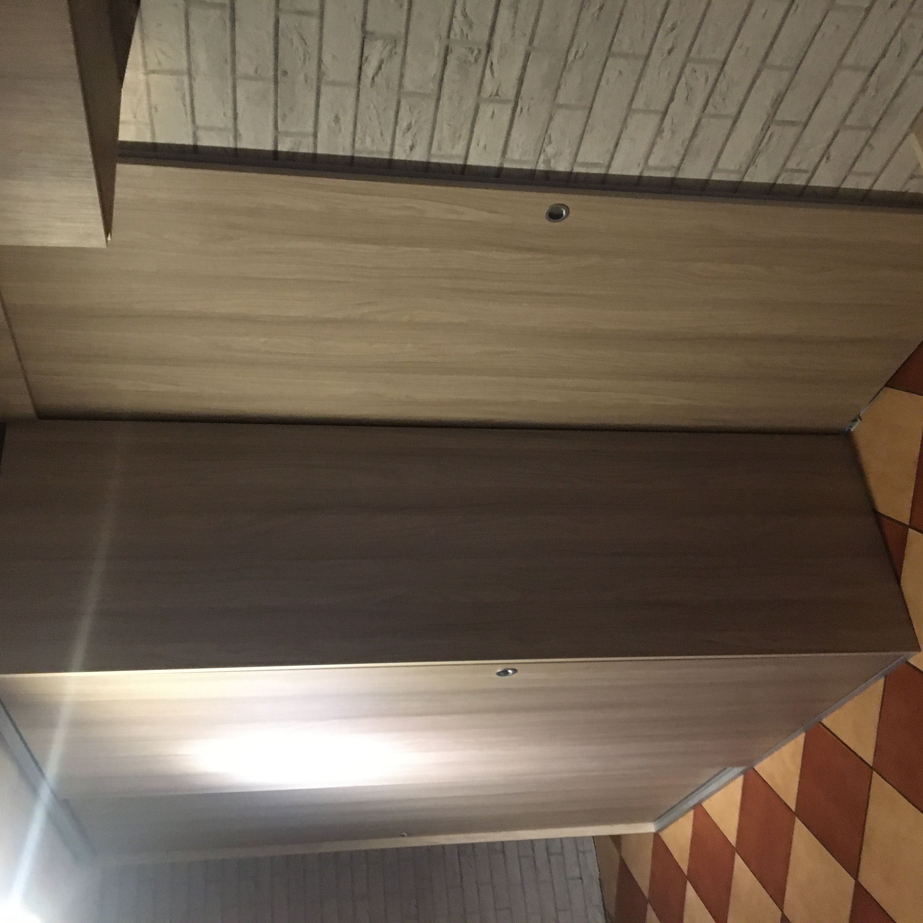 Fragment szafy z przesuwnymi drzwiami, widoczny fragment ściany z białej cegły i fragment podłogi w brązowo-beżową szachownicę.