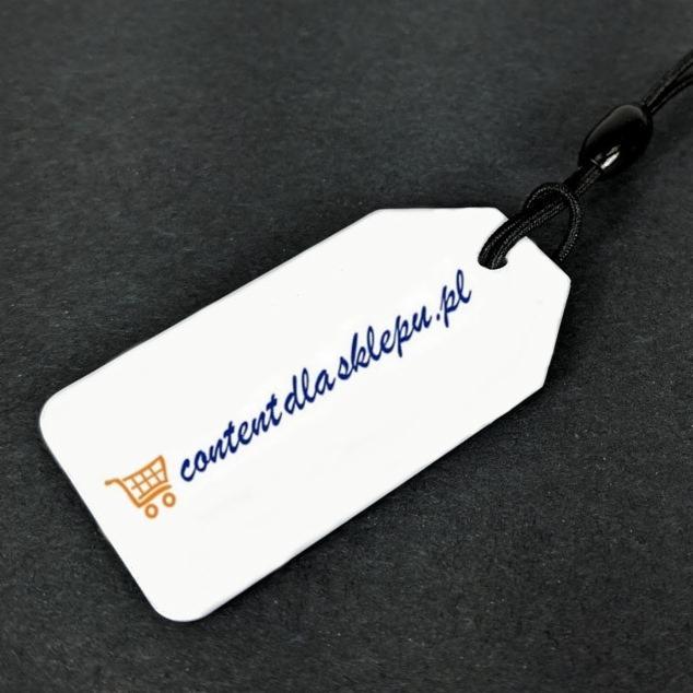 Biała metka z napisem 'content dla sklepu.pl' i ikoną wózka sklepowego, zawieszona na czarnym sznurku na ciemnym tle.