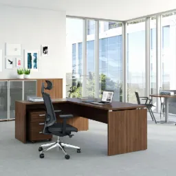 Nowoczesne biuro z biurkiem narożnym w odcieniach brązu, ergonomicznym krzesłem obrotowym, szafką z przeszklonymi frontami i dekoracjami ściennymi w jasnym pomieszczeniu z dużymi oknami.