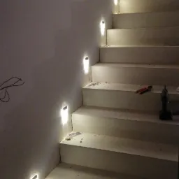 Schody z podświetleniem LED w ścianie, widoczne przewody elektryczne i narzędzia, etap montażu.