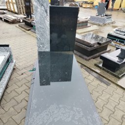 KAM-TAX - Części nagrobków z czarnego i szarego granitu, ułożone na zewnątrz, czekające na montaż. W tle budynek i palety z kamieniami.