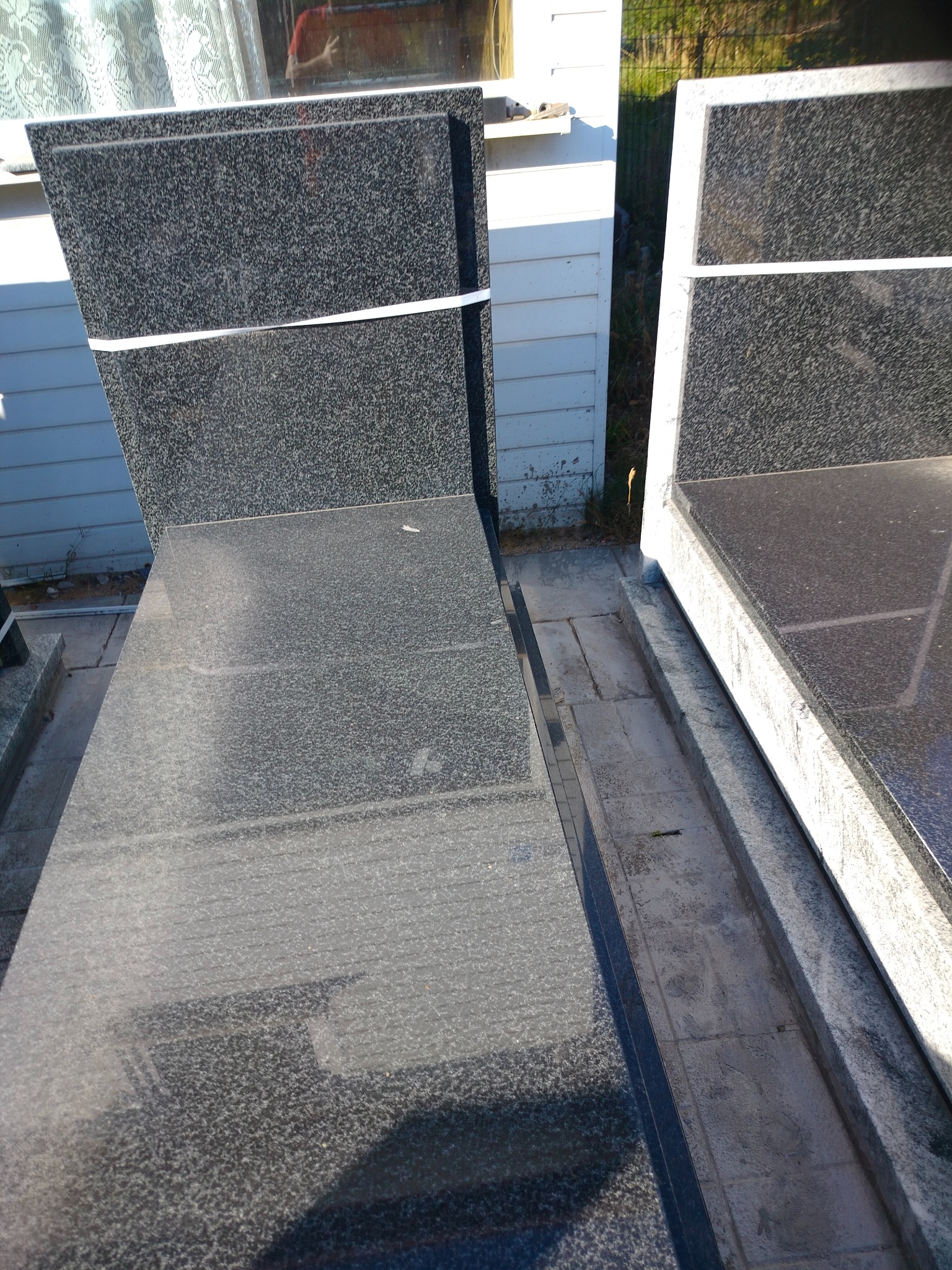 Ciemne, polerowane płyty kamienne z granitu, zabezpieczone taśmą, ustawione pionowo na zewnątrz. Widoczne krawędzie i faktura kamienia.