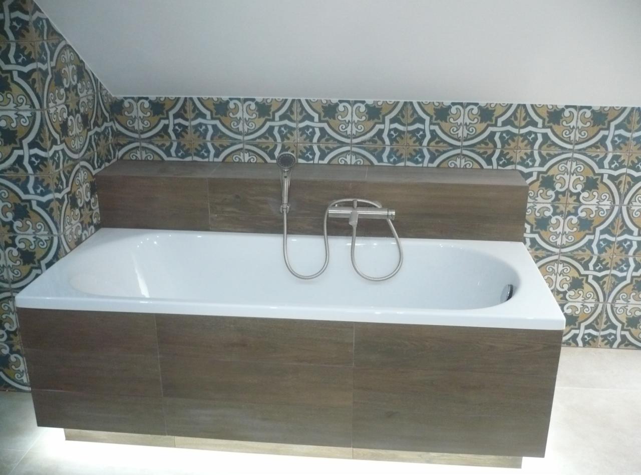 Biała wanna obudowana brązowymi płytkami imitującymi drewno, z ozdobną, wzorzystą glazurą na ścianie i podświetleniem LED u dołu obudowy.