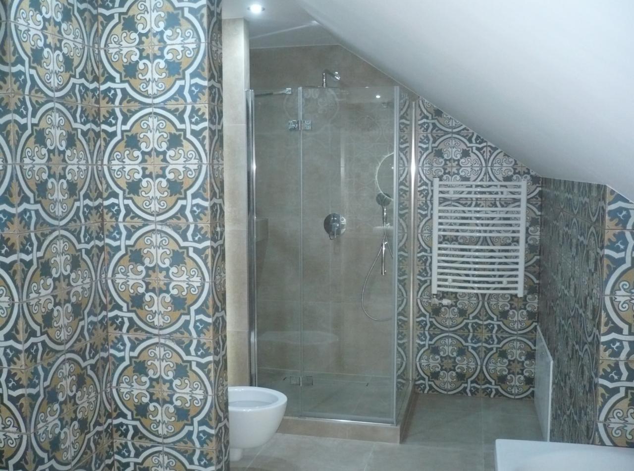 Wykończona łazienka na poddaszu z kabiną prysznicową ze szklanymi drzwiami, grzejnikiem drabinkowym i toaletą, wyłożona dekoracyjnymi płytkami w stylu marokańskim z motywem kwiatowym w odcieniach...