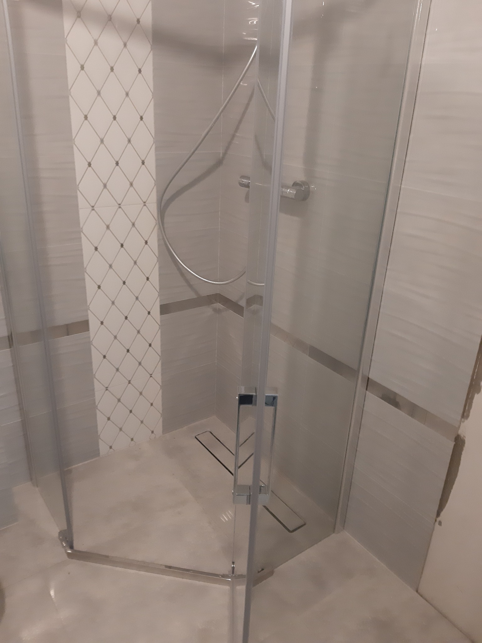 Nowoczesna kabina prysznicowa z odpływem liniowym w posadzce, wykończona jasnymi płytkami z dekoracyjnym pasem w romby.