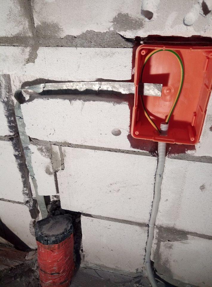 Pomarańczowa puszka elektryczna w ścianie z gazobetonu, widoczne przewody zasilające i peszel, przygotowanie do montażu gniazdka.