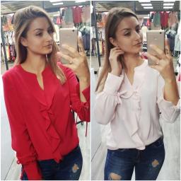 Firma Regina Beata Wójcik, Jarosław Wójcik Spółka Cywilna - Selfie w lustrze prezentujące dwie bluzki z falbanami: czerwona i pudrowo-różowa, z rękawami zakończonymi wiązaniem, na tle wieszaków z ubraniami.