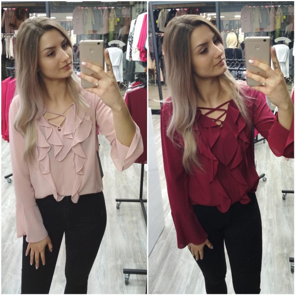 Kobieta robi selfie w lustrze, prezentując dwie bluzki z falbanami w kolorach pudrowego różu i burgundu, z wiązaniem na dekolcie i rozszerzanymi rękawami, w tle widać wieszaki z ubraniami.