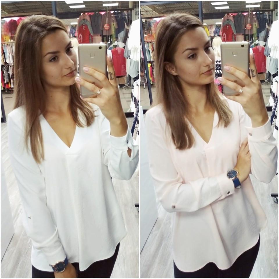 Selfie młodej kobiety w dwóch bluzkach z długim rękawem, biała i pudrowo-różowa, na tle wieszaków z odzieżą w sklepie.