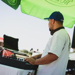 Everyday Events Filip Tucki - DJ w niebieskiej czapce obsługuje mikser Traktor na zewnątrz, pod zielonym parasolem reklamowym, z widocznym food truckiem w tle.