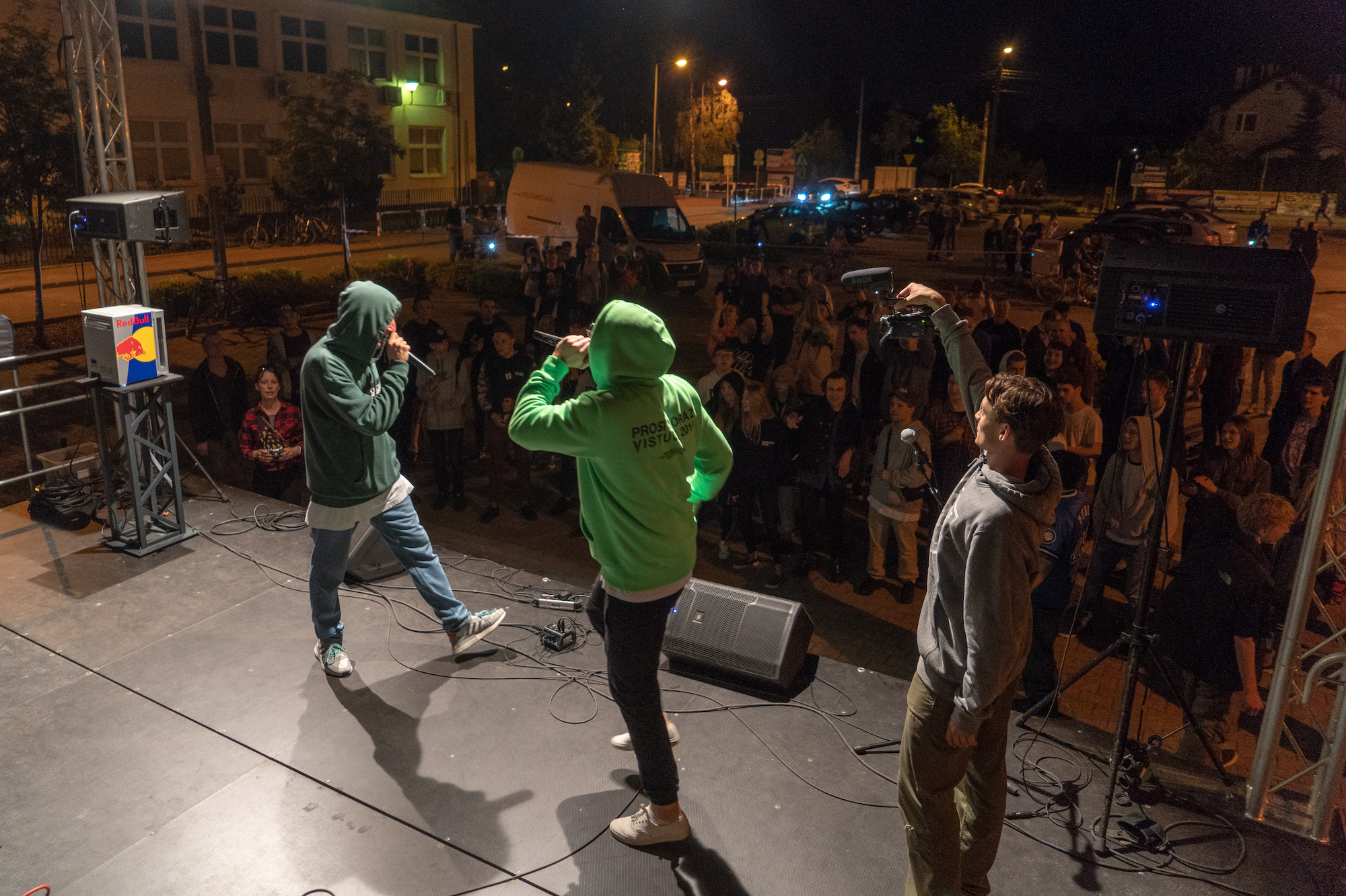 Występ raperów na scenie podczas plenerowego koncertu, oświetlenie sceniczne, publiczność w tle, nagrywanie występu kamerą z mikrofonem Rode.