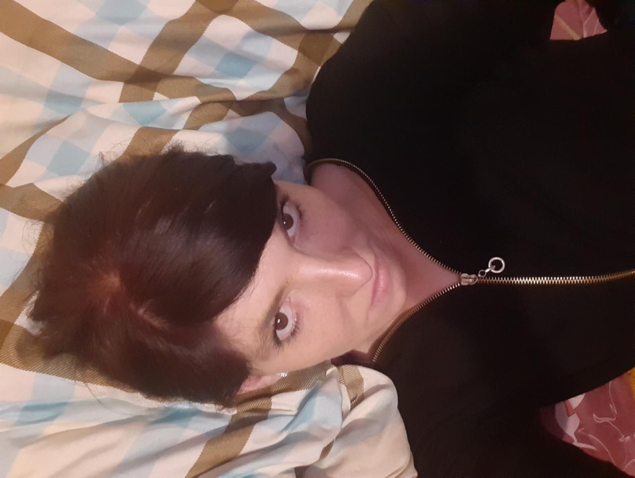 Kobieta leżąca na łóżku w czarnej bluzie z suwakiem, patrząca w górę, z widocznymi brązowymi włosami i fragmentem wzorzystej pościeli.