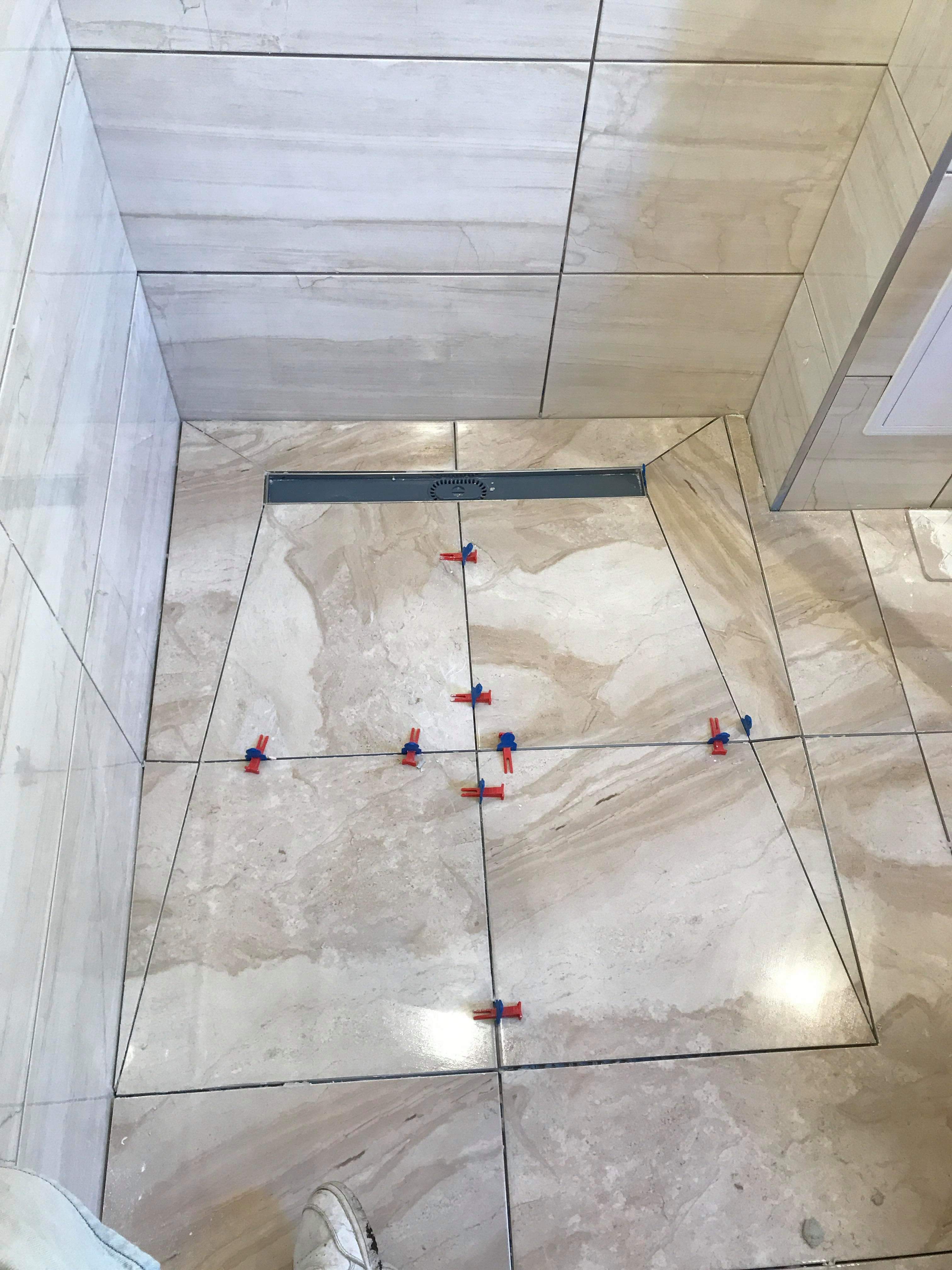 Ułożone płytki podłogowe w łazience z odpływem liniowym, widoczne krzyżyki dystansowe, neutralna kolorystyka płytek imitująca marmur.