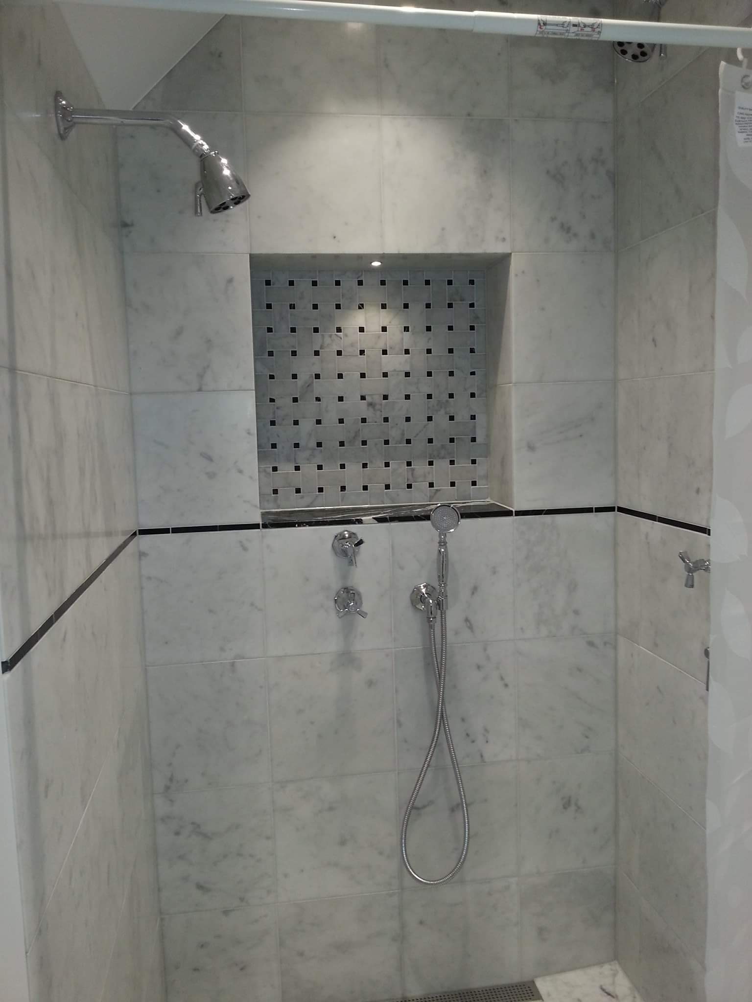 Wykończona kabina prysznicowa z marmurowymi płytkami, czarnymi akcentami i wnęką z mozaiką.