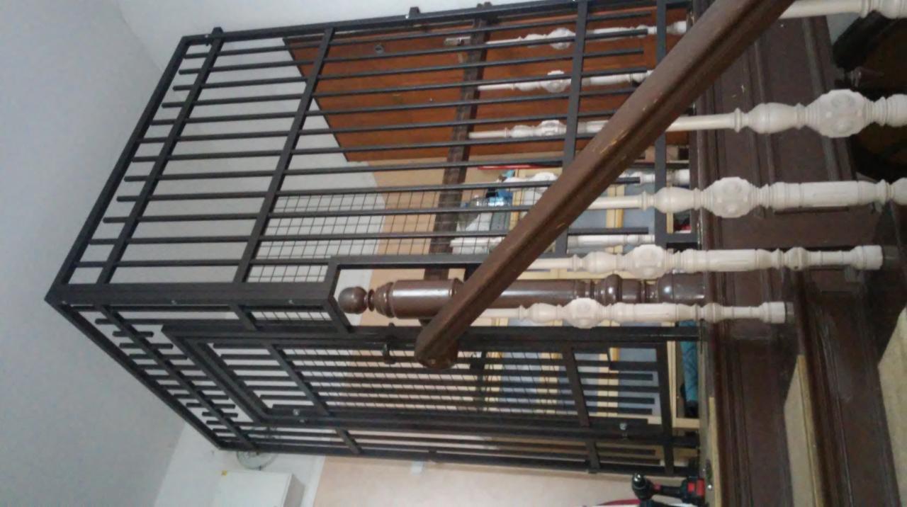 Metalowa konstrukcja ogrodzenia panelowego, widoczna z dołu, z fragmentem drewnianej balustrady schodów w tle.