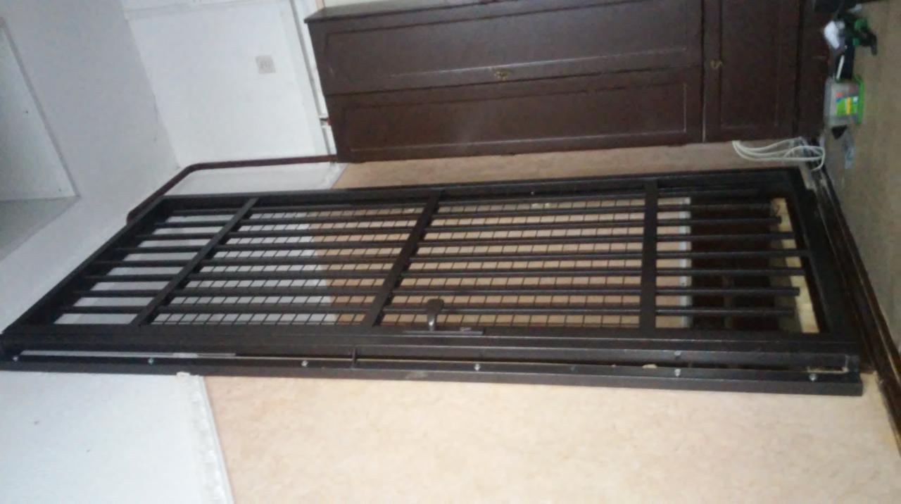 Rozłożony, brązowy panel ogrodzeniowy z metalowymi prętami, leżący na podłodze w pomieszczeniu, z widoczną szafką w tle.