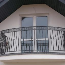 Patryk Andrzejewski - Kuty balkon z geometrycznym wzorem greckim na górnej listwie, zamontowany przy oknie na poddaszu domu.