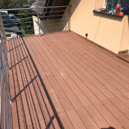 Nowoczesny taras z desek kompozytowych w odcieniach brązu, z balustradą ze stali nierdzewnej, widok z g&oacute;ry na ukończoną realizację.